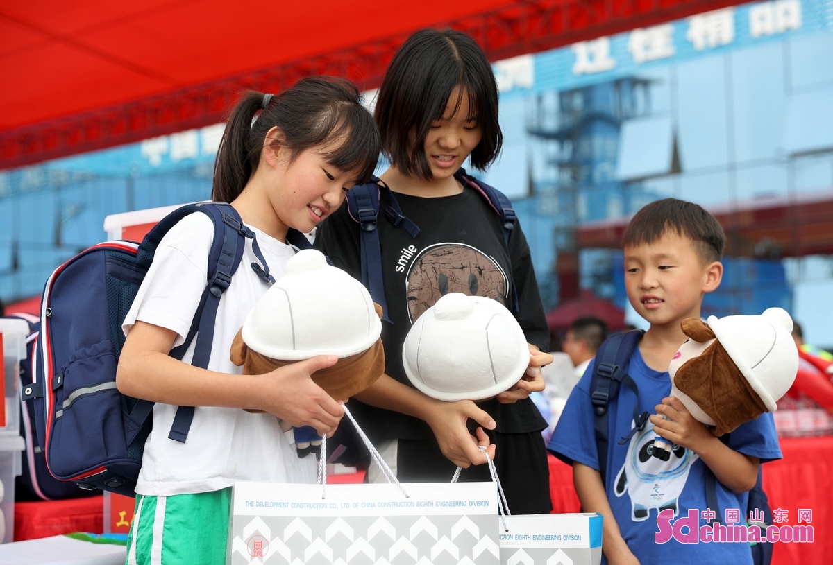 <br/>　　7月21日，在中建八局青岛上合示范区项目工地，三名留守儿童在翻看刚刚获赠大礼包。(张进刚 摄)<br/>　　